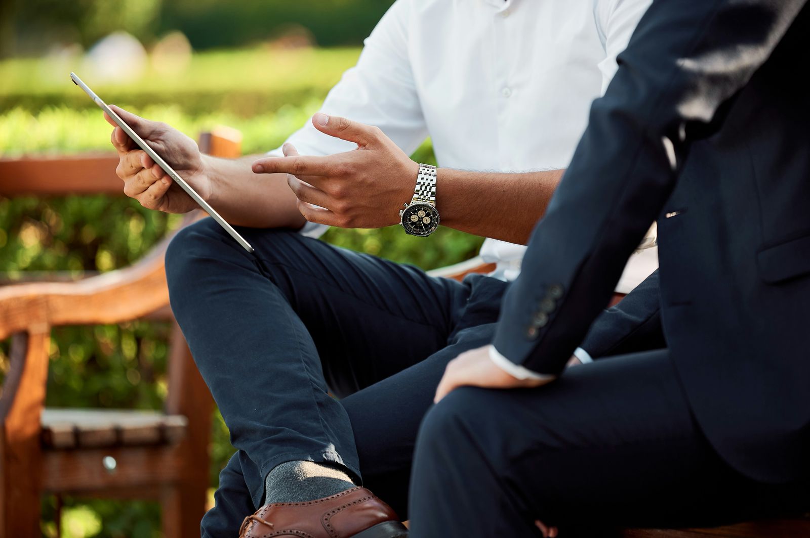 Two business people in conversation on a bench, one holding a tablet