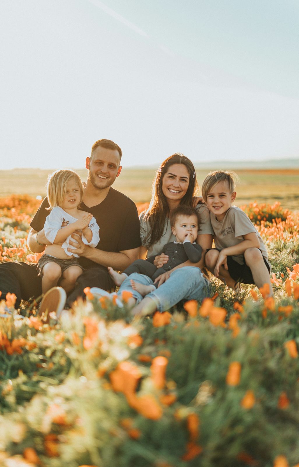 Family of five relaxing together in a field of orange poppies