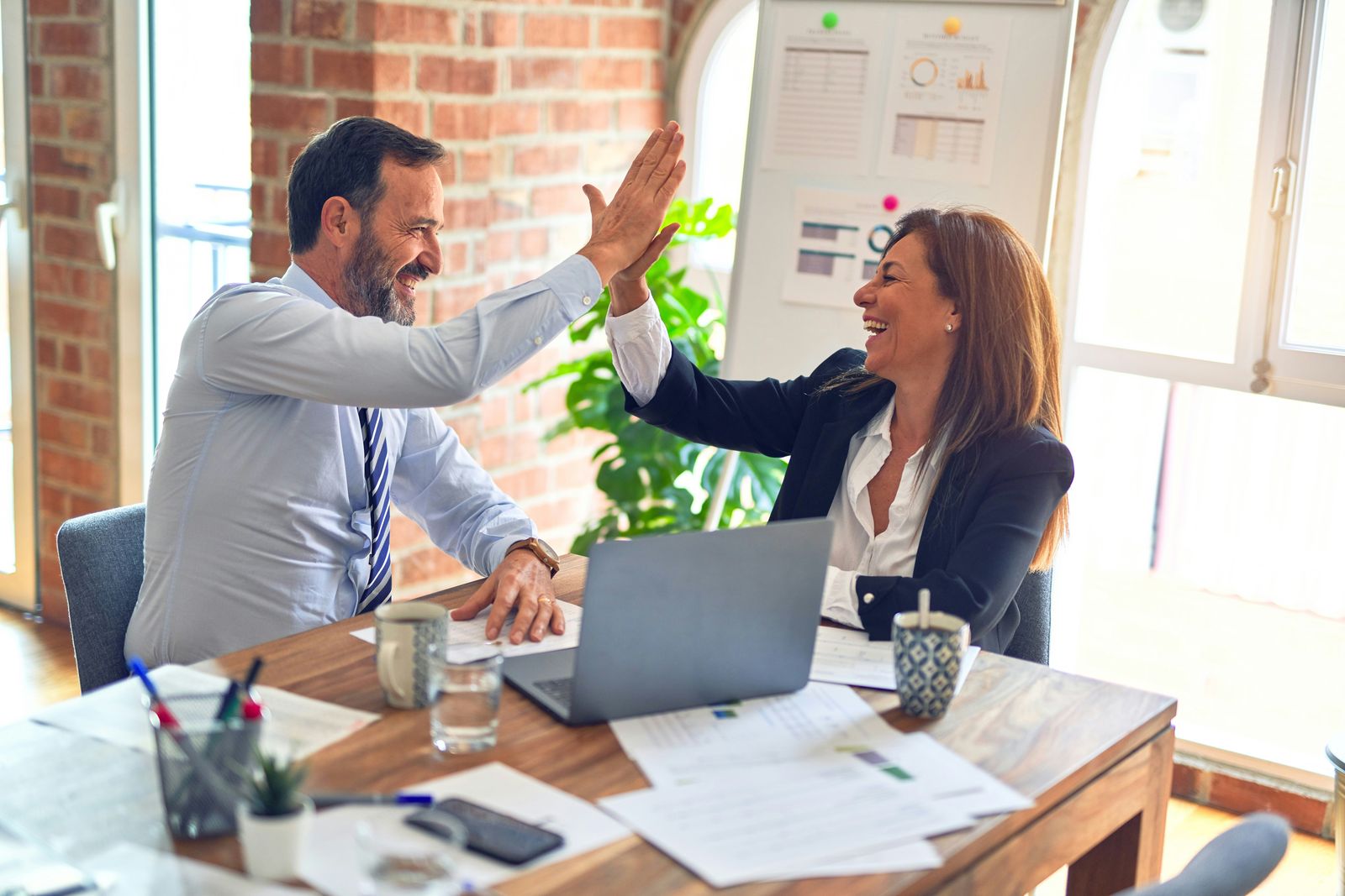 Two colleagues sharing a high five at an office desk with a laptop